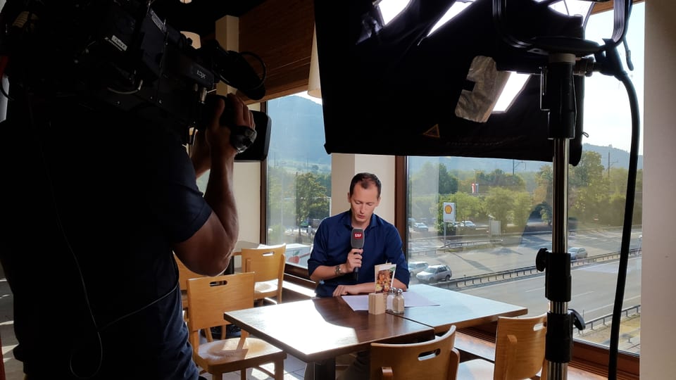 Michael Weinmann schaut an einem Tisch auf ein Papier, Autobahn im Hintergrund, Licht und Kameramann vorne