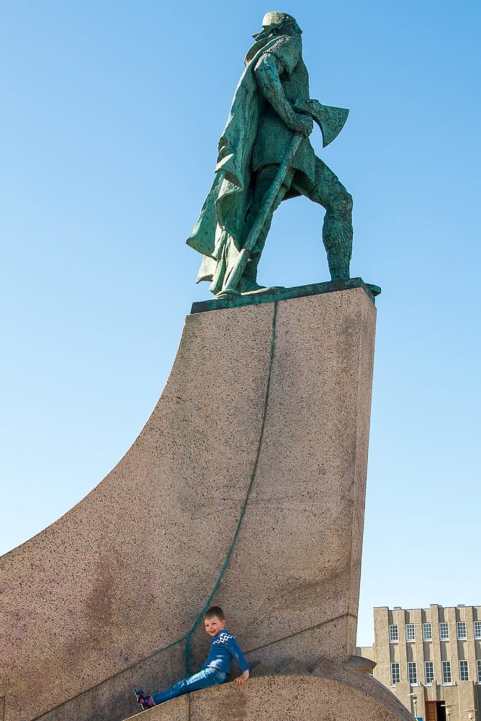 Ein Bub sitzt am Fusse der Statue von Leifur Eiríksson.