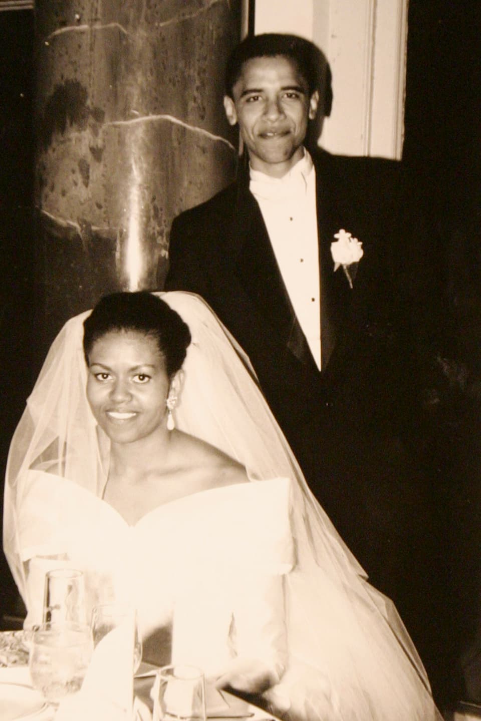 Michelle Obama sitzend im Hochzeitskleid und Barack Obama stehend im Smoking.
