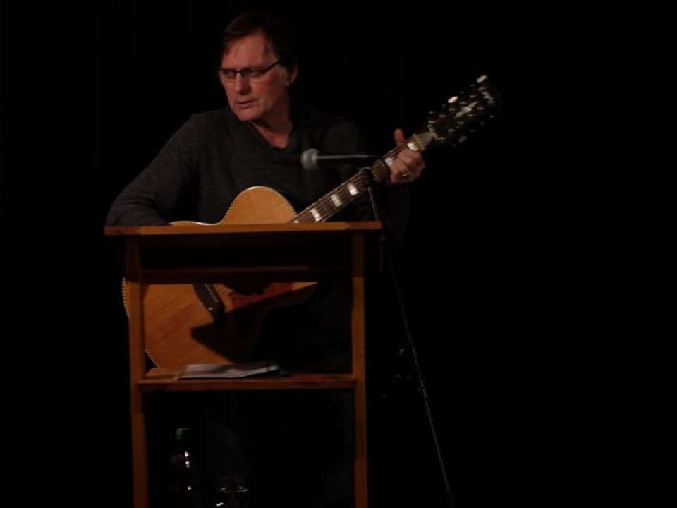 Mann auf dunkler Bühne mit Gitarre.