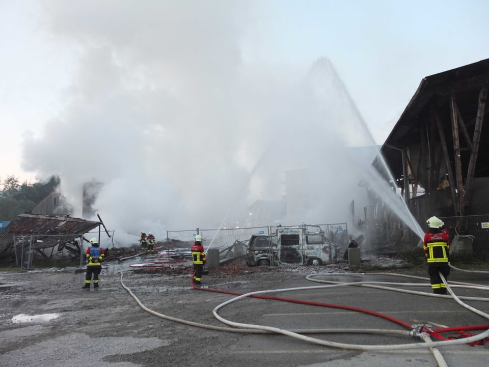 Feuerwehrleute vor Ruine, ein ausgebrannter VW-Bus im Vordergrund