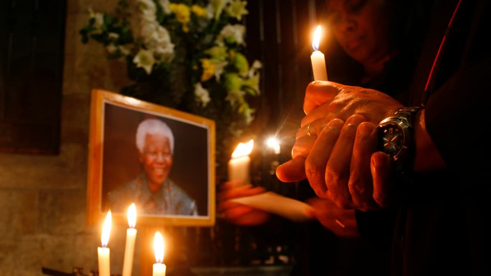 Zwei Menschen mit Kerzen in stiller Andacht vor einem Portrait des lächelnden Mandelas.
