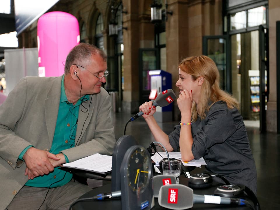 Moderator Andreas Müller-Crepon und Lara Stoll mit Mikrophonen an einem Stehtisch. 