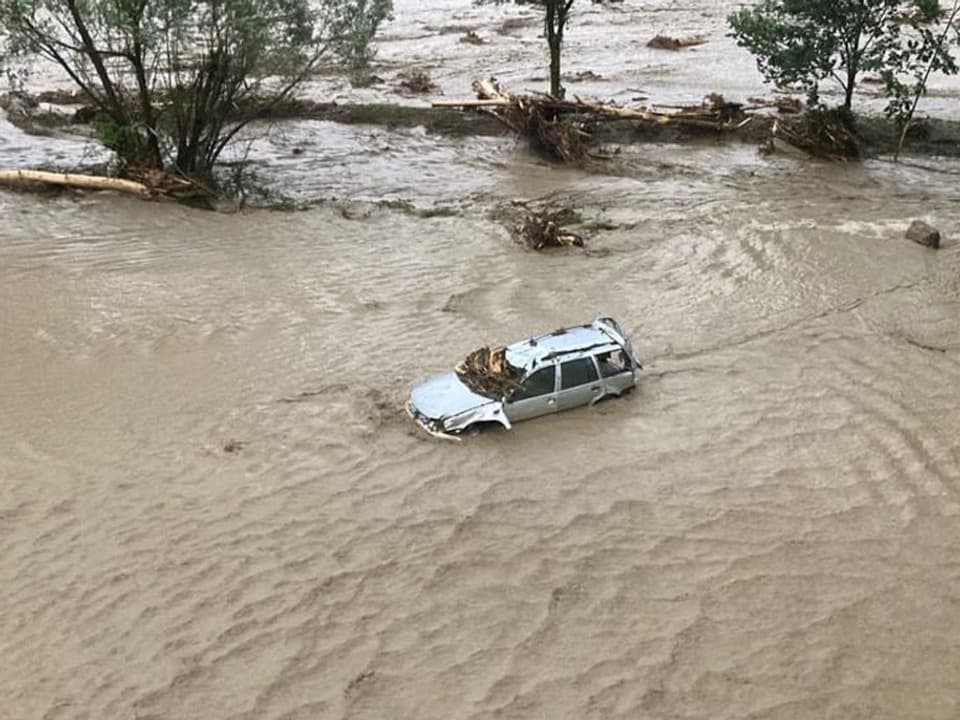 Ein Auto schwimmt im braun gefärbten Wasser, das bis zu dessen Scheiben hervorragt.