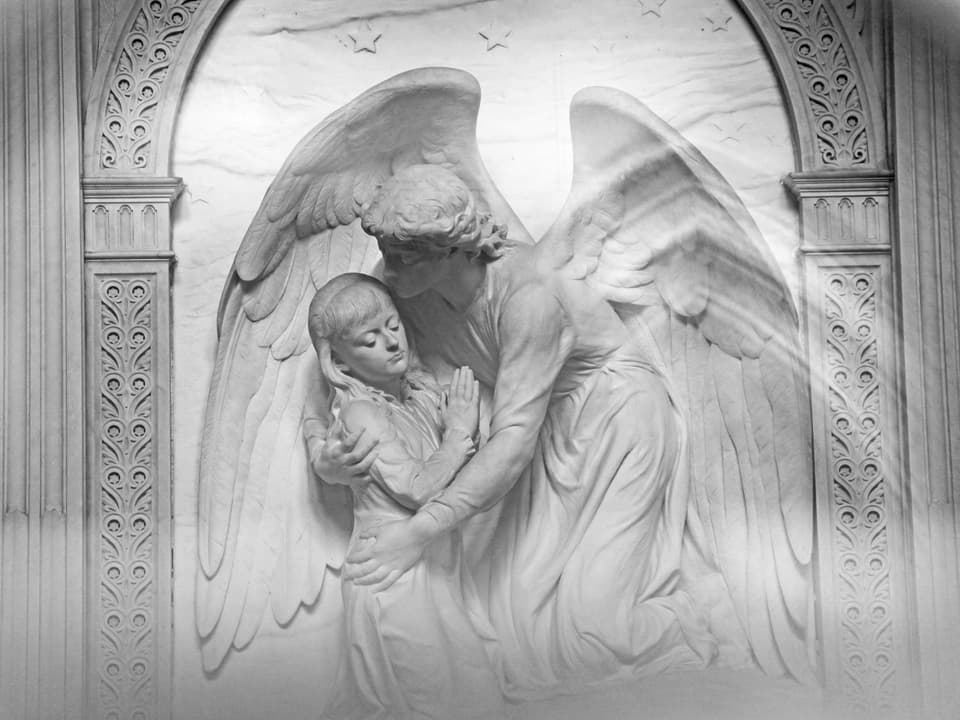 Ein weisser Engel aus Marmor umarmt ein kleines Mädchen.