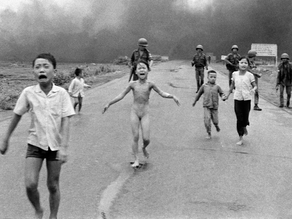 Kinder rennen von einer dunklen Wolke davon. In der Mitte ein nacktes Mädchen, das vor Angst schreit. Im Hintergrund Soldaten. 