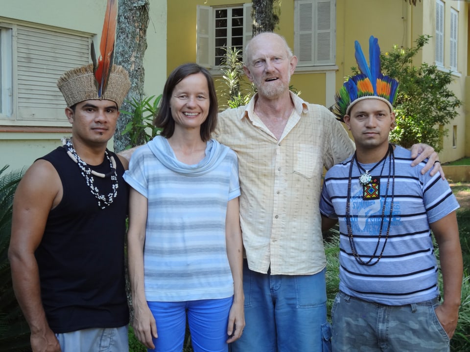 Ein Gruppenfoto mit vier Menschen, zwei tragen Federschmuck auf dem Kopf.