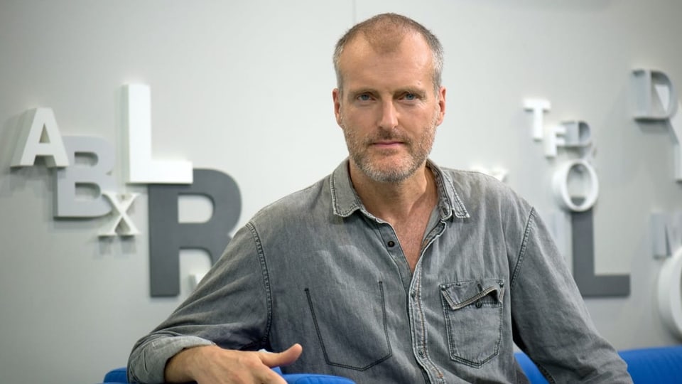 Ein Mann mit Bart im grauen Hemd.