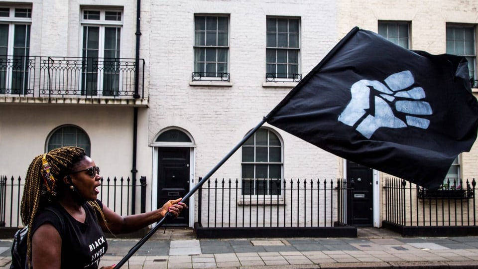 Eine schwarze Frau demonstriert und hält eine Flagge mit einer weissen Faust.