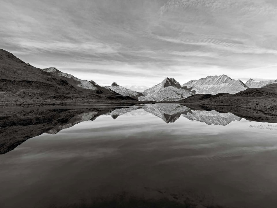Schwarzweissbild: In einem klaren Bergsee spiegelt sich eine Gebirgskette.