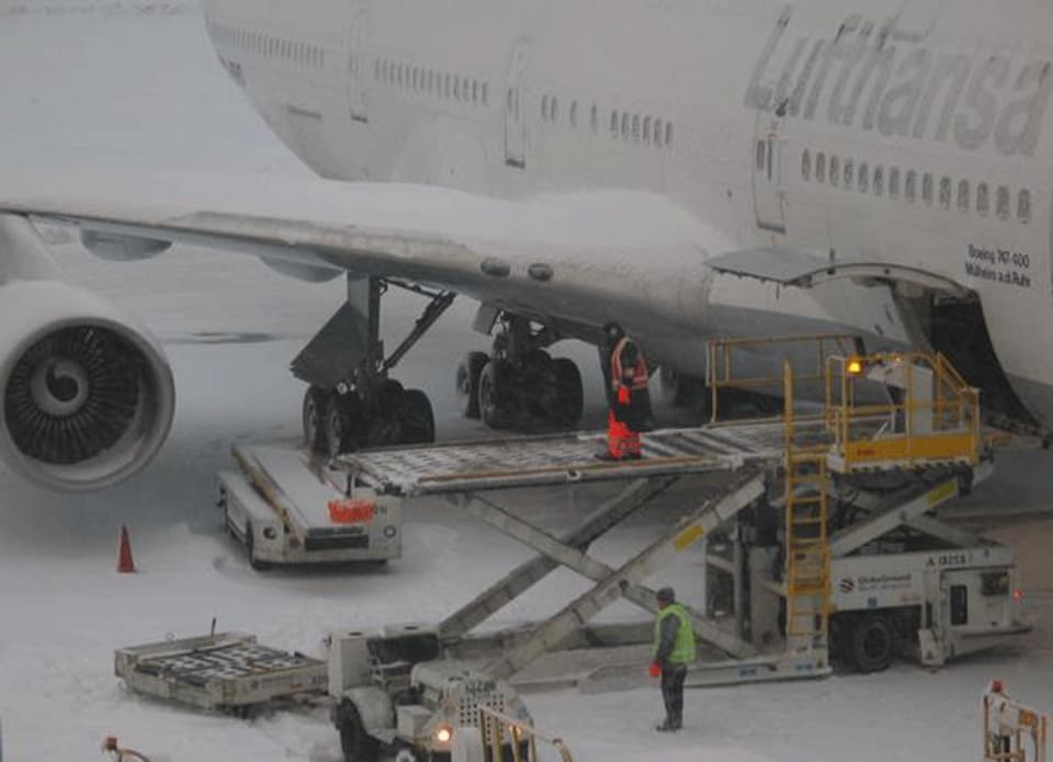 Zwei Angestellte arbeiten neben einem schneebedeckten Lufthansa-Flugzeug