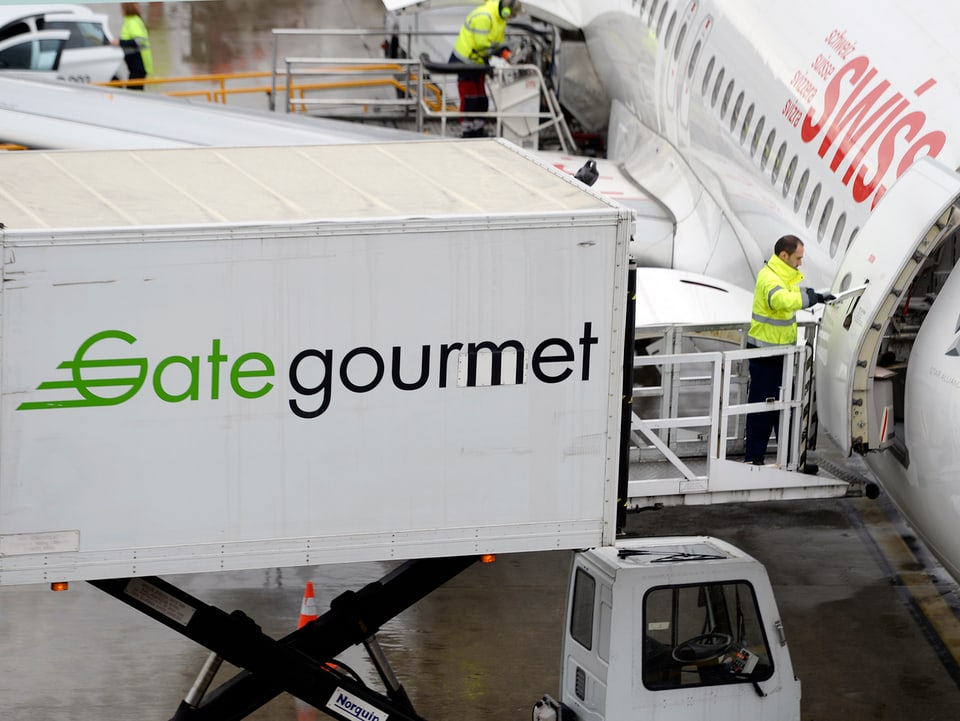 Container mit der Aufschrift Gate Gourmet auf einer Hebebühne vor einem Siwss-Flugzeug