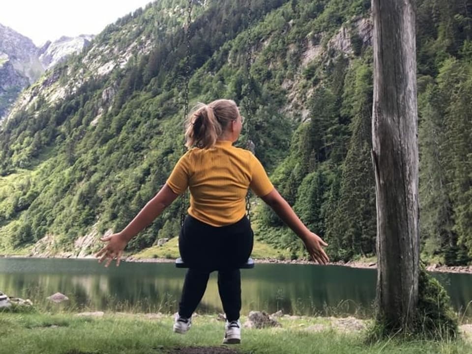 Ein älteres Mädchen auf eine Schaukel mit Blick auf einen Bergsee.