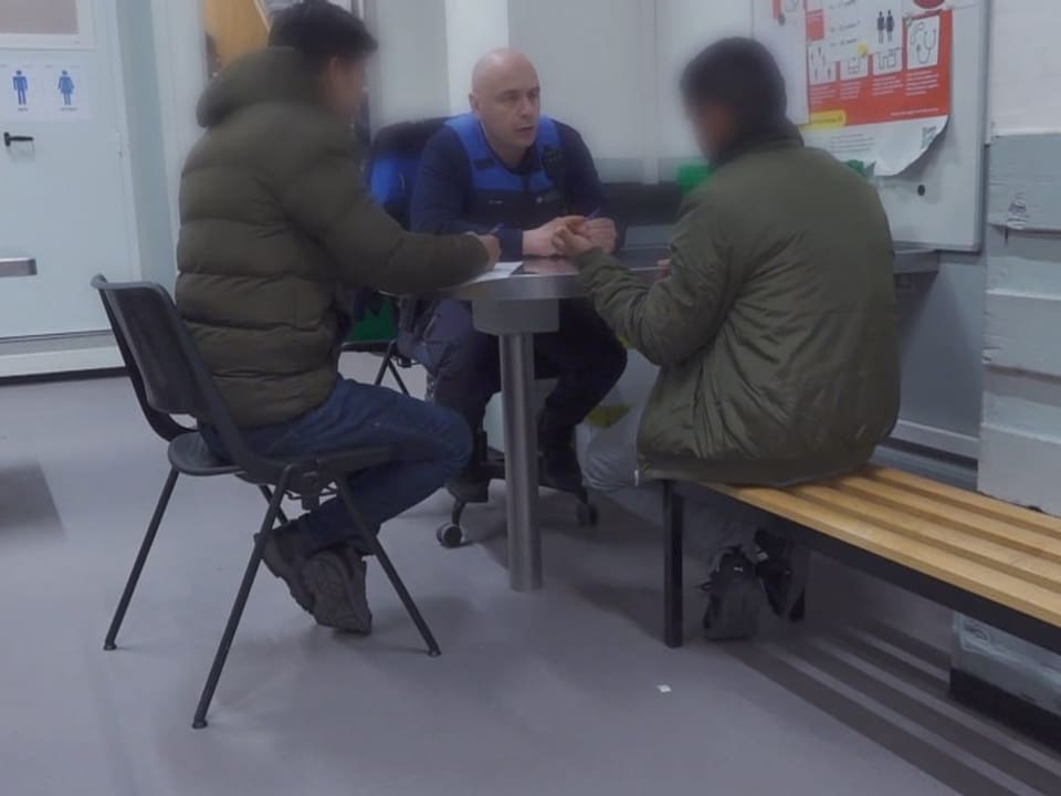 Zwei Flüchtlinge sitzen einem Grenzschutzbeamten gegenüber. 