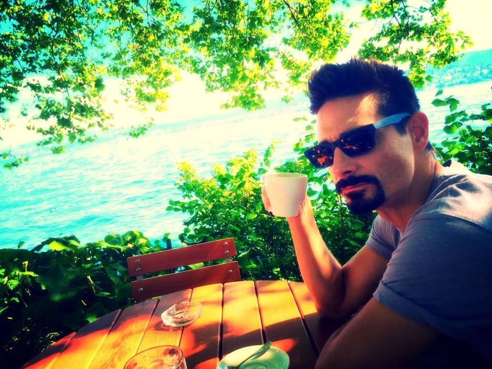 Kevin Richardson mit einer Tasse Kaffee am See an einem Tisch sitzend.