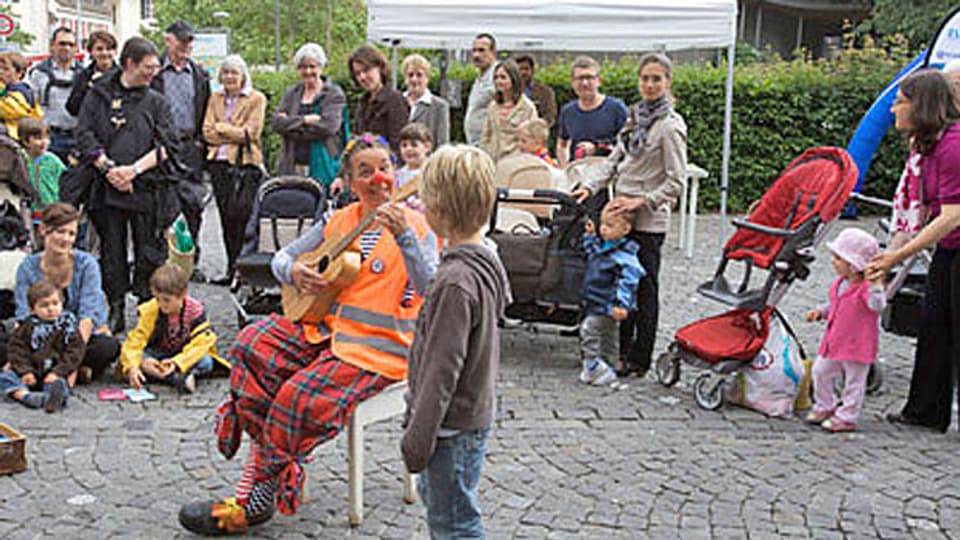 Eine Clownin spielt Gitarre auf einem Platz in der Altstadt, umringt von Kindern.