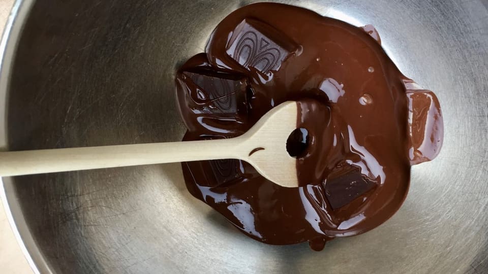 Eine Metallschüssel mit schmelzender schwarzer Schokolade.