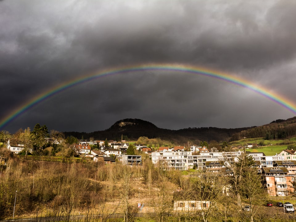 Im Vordergrund Häuser am Südhang von Sissach. Auf dem Hügel trohnt die Sissacher Fluh unter einem prachvollen Regenbogen.