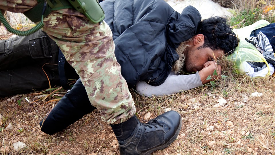 Ein tunesischer Flüchtling liegt am Boden. Über ihm steht ein italienischer Soldat.