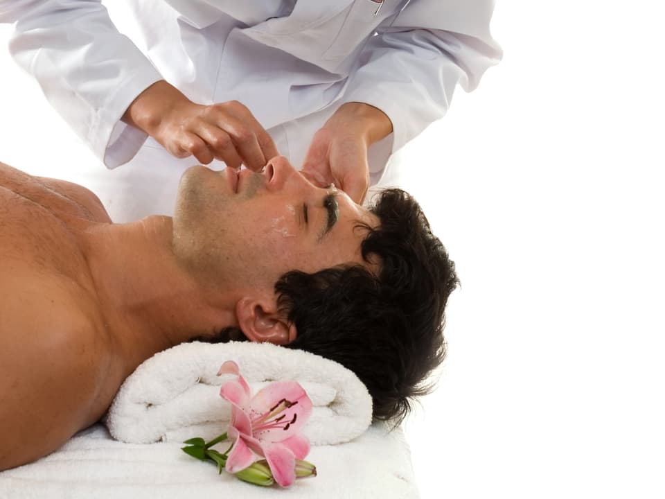 Ein Mann liegt auf dem Rücken, Augen geschlossen, erhält eine Kosmetikbehandlung.