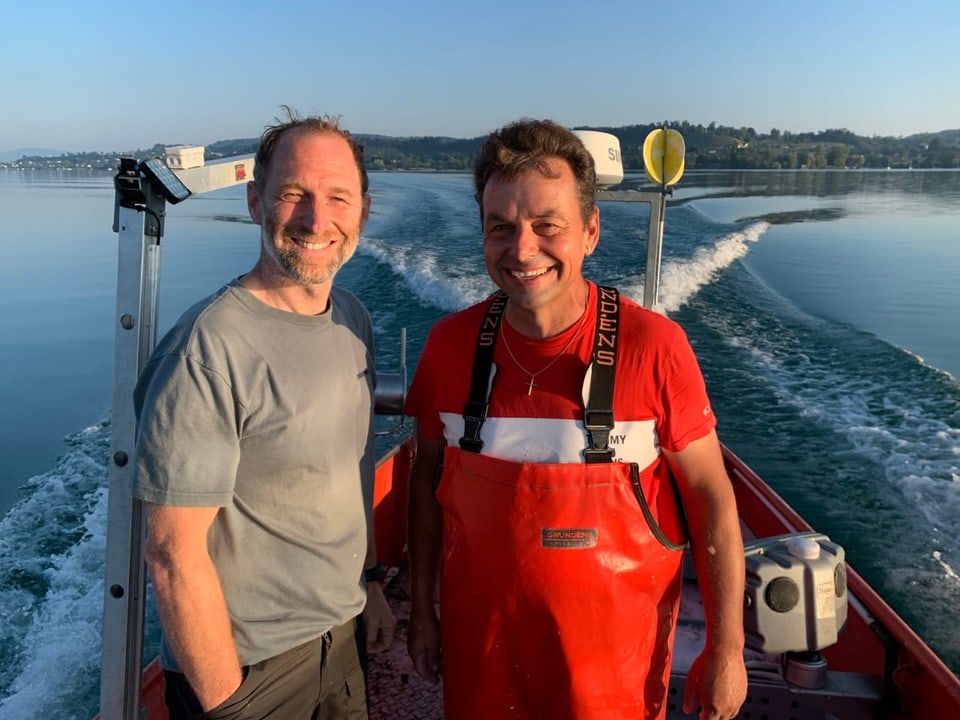 2 Männer auf fahrendem Boot lächeln in die Kamera