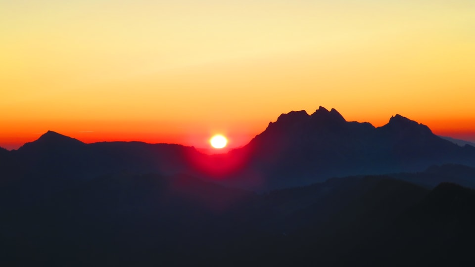 Die Sonne taucht um 05.30 Uhr links neben dem Pilatus auf, der Himmel leuchtet am Horizont rot und orange. Die Sonnenscheibe steht knapp über der Bergkette. 