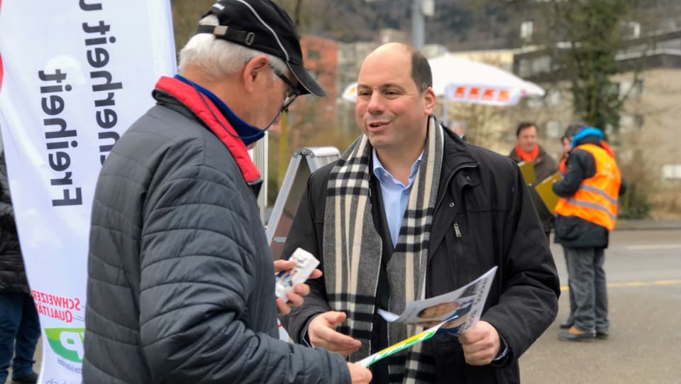 SVP-Nationalrat und Präsident der SVP Stadt Zürich verteilt Flyer an einen älteren Passanten. 