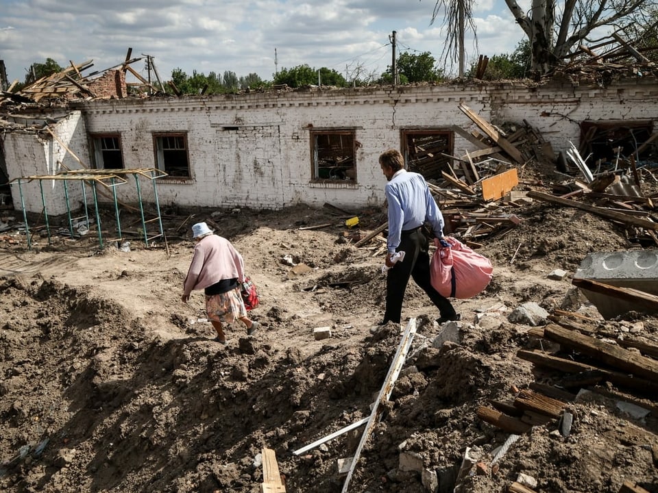 Ein Mann und eine Frau gehen an einer zerstörten Schule in der Frontstadt Orikhiv, Oblast Saporischja, vorbei.