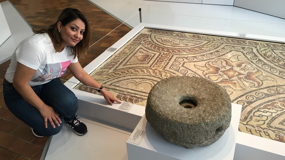 Sherin Abdulhannan kniet vor einer Handmühle im Museum zu Allerheiligen 