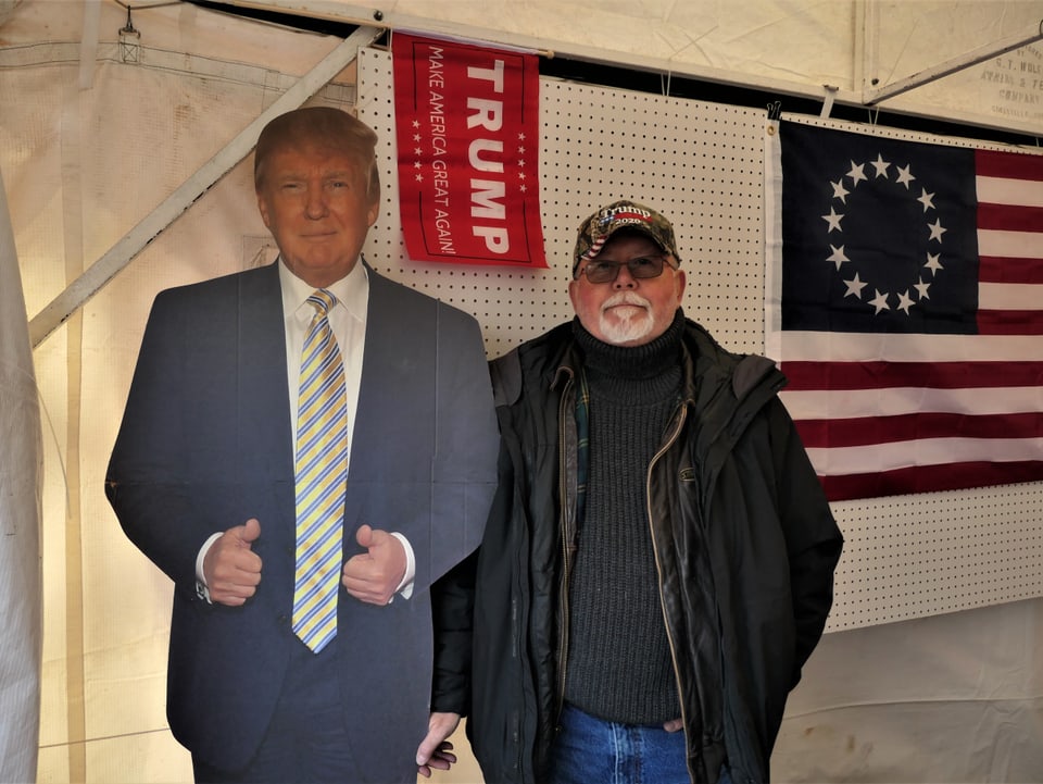 Eine Person steht neben einer Trump-Figur aus Pappe.