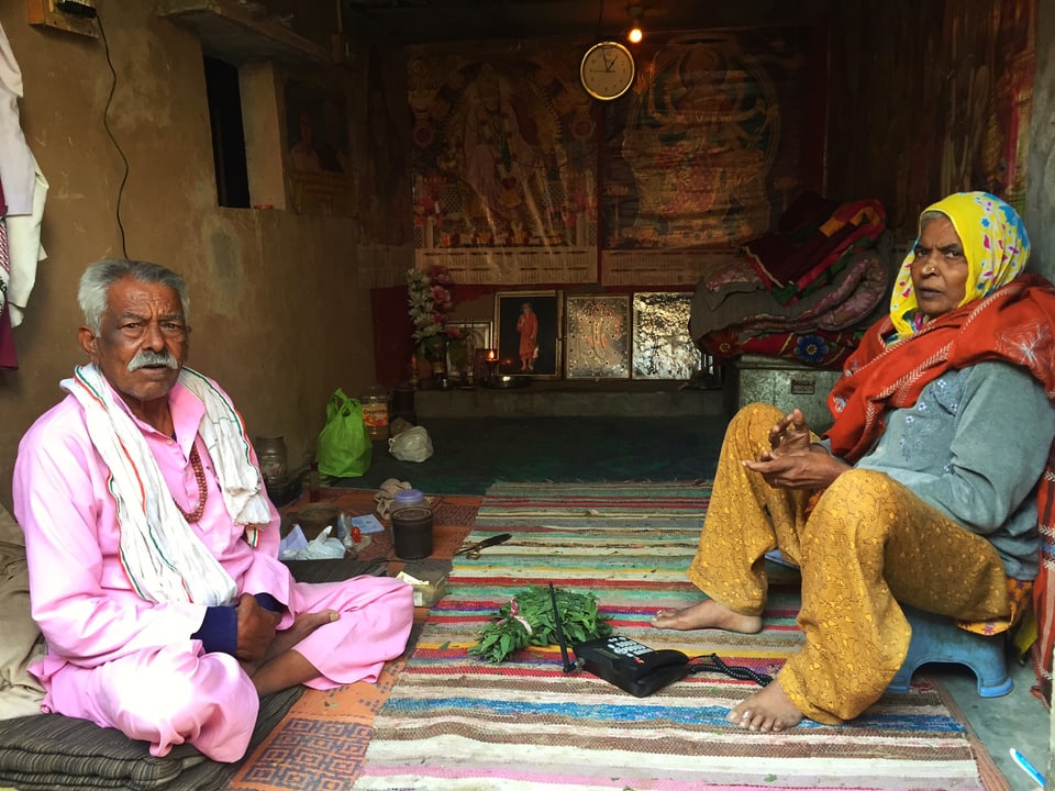 Ein älteres Paar sitzt auf dem Boden in seiner Hütte.