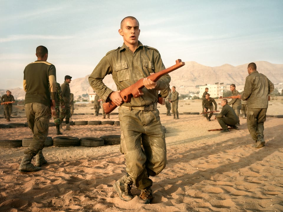Ein Soldat läuft mit einem Gewehr in der Hand auf dem Sand.