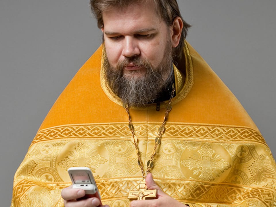Ein Priester im gelben Gewand blickt auf sein Mobiltelefon.