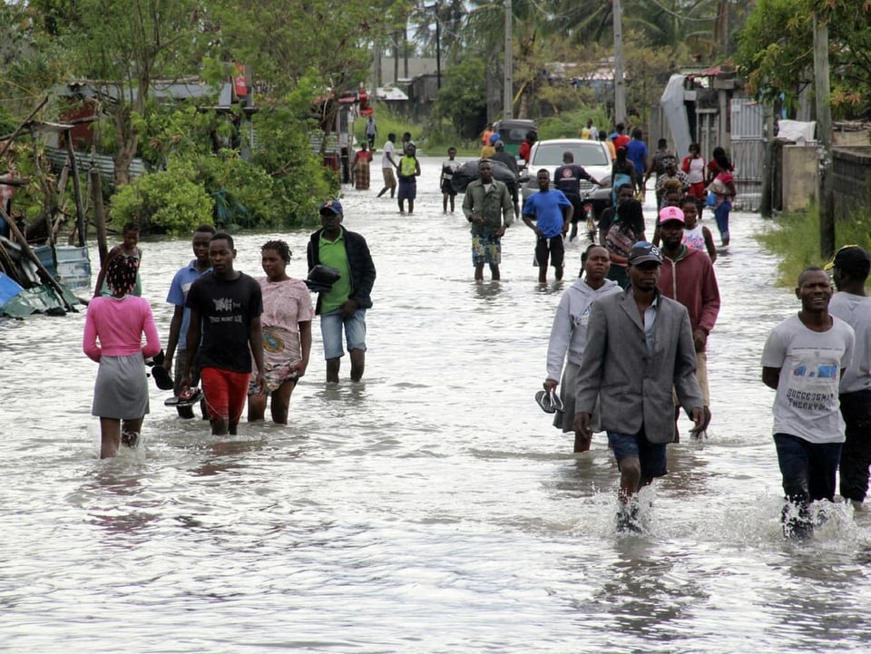 Menschen waten durch eine überschwemmte Strasse.