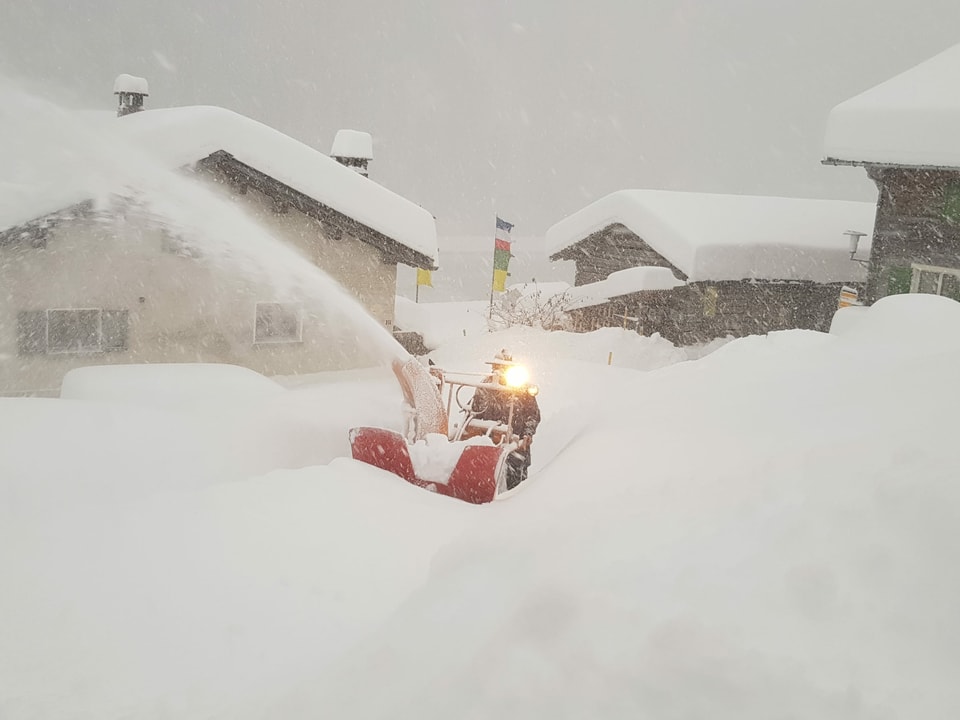 Ein Mann räumt einen Weg mit einer Schneefräse in einem tief verschneiten Dorf.