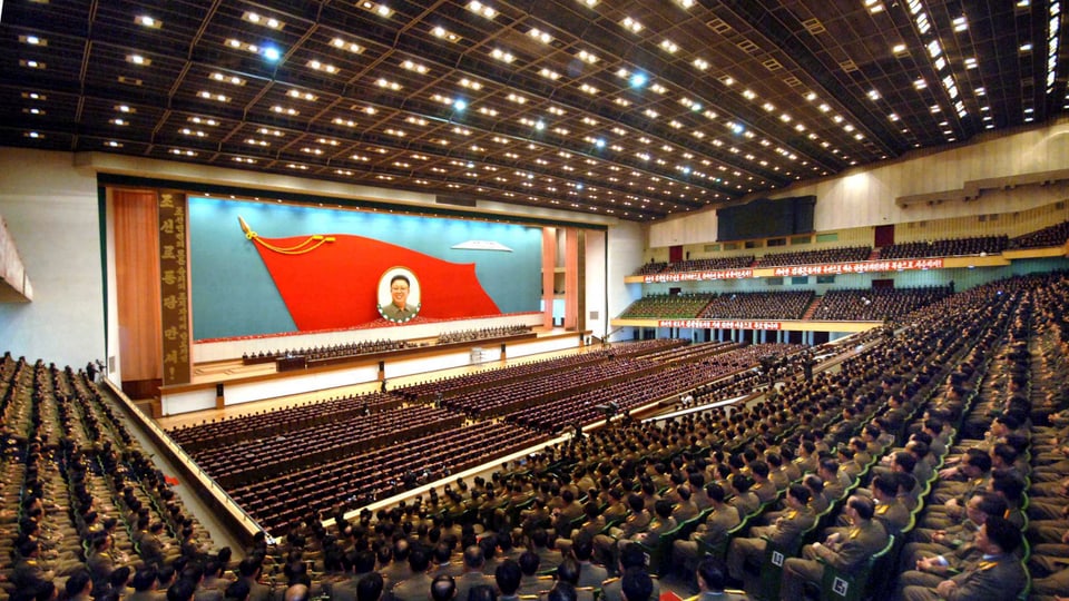 grosse Halle mit hunderten Militärs und Staatsdienern, im Hintergrund das Portrait von Kim Jong Il.