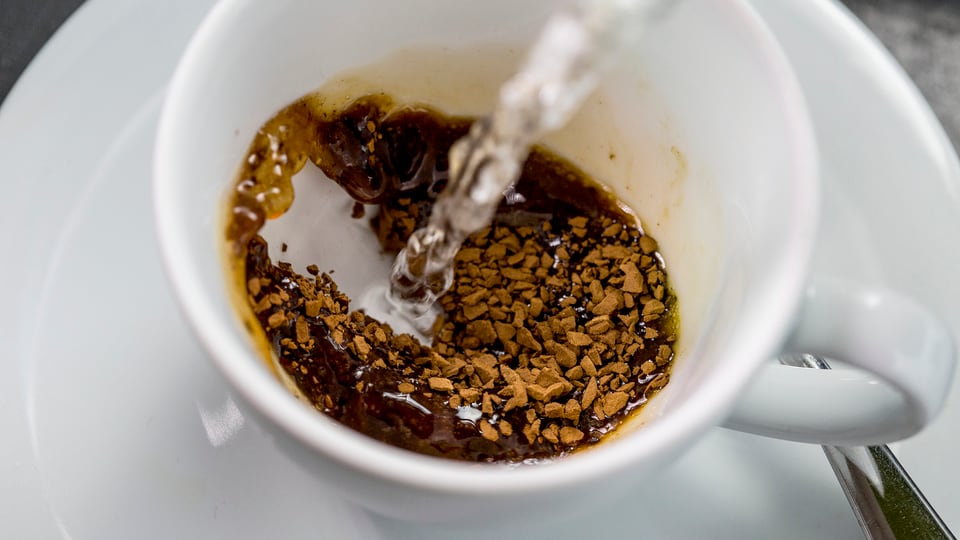 Löslicher Nescafé in einer Tasse. Heisses Wasser wird hinzugeschüttet.