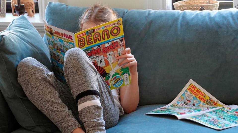 Kind auf Sofa, vertieft in einen Comic namens «Beano».