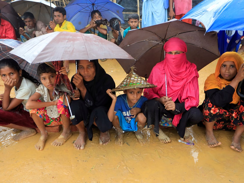 Menschen sitzen in einem Flüchtlingslager im Regen auf dem Boden.