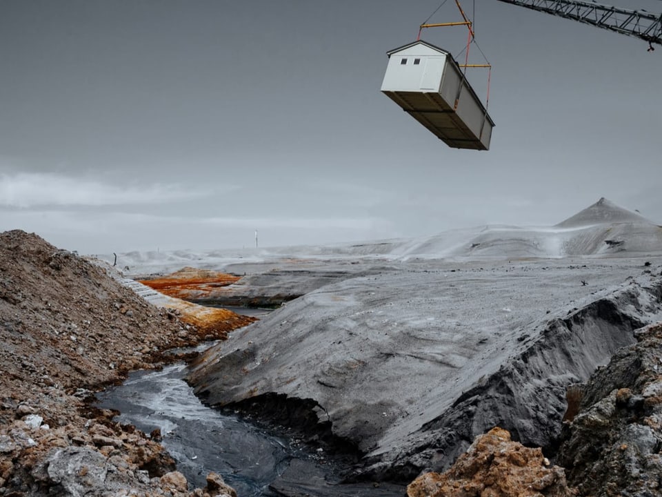 Fotografie einer Kraterlandschaft und ein Kran lässt ein Haus herab