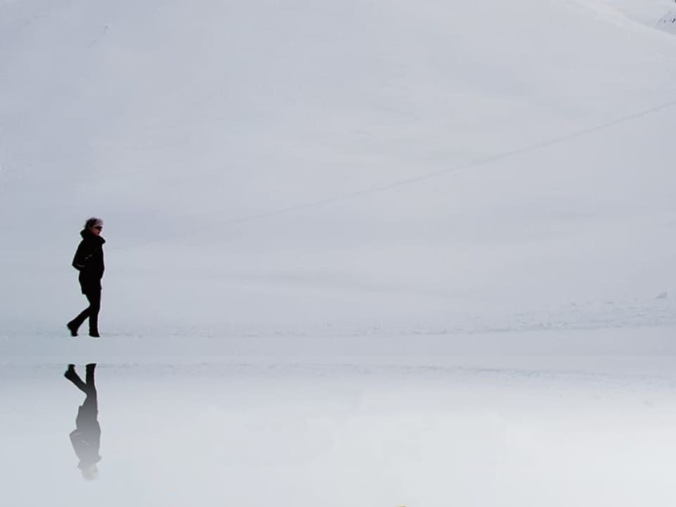 Frau läuft an einem verschneiten, zugefrorenen Seeufer entlang.