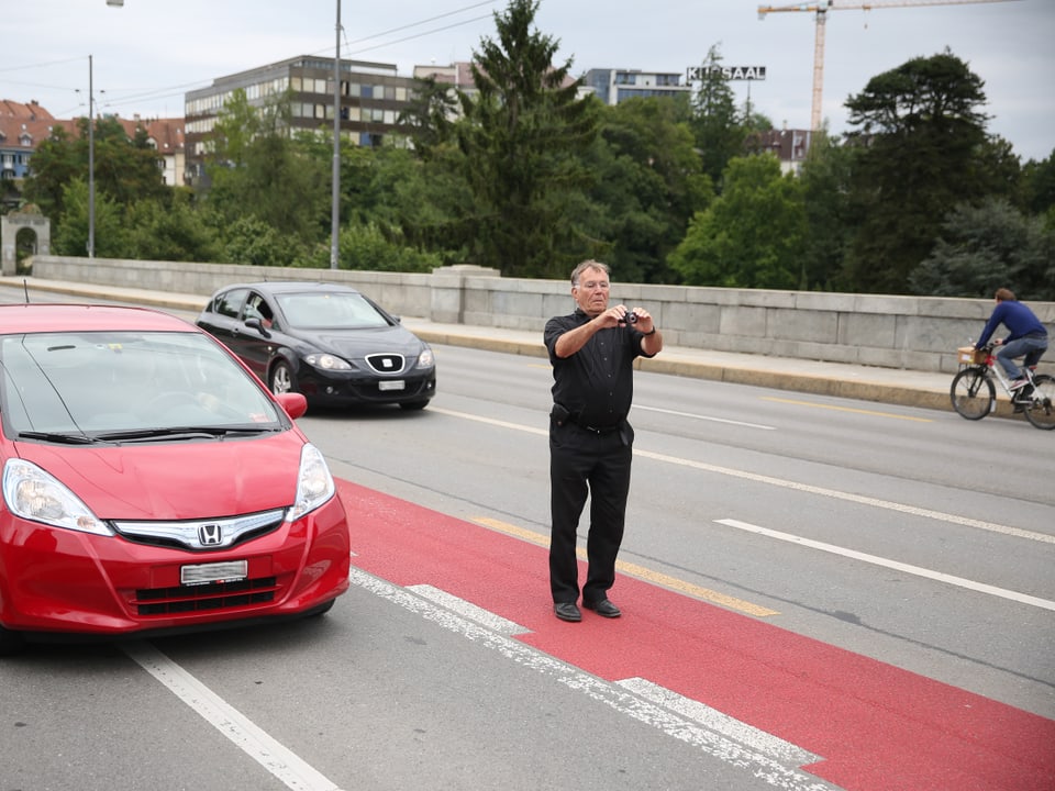 Jan Gehl steht auf dem roten Velostreifen inmitten der Strasse, fotografiert, Autos fahren an ihm vorbei.