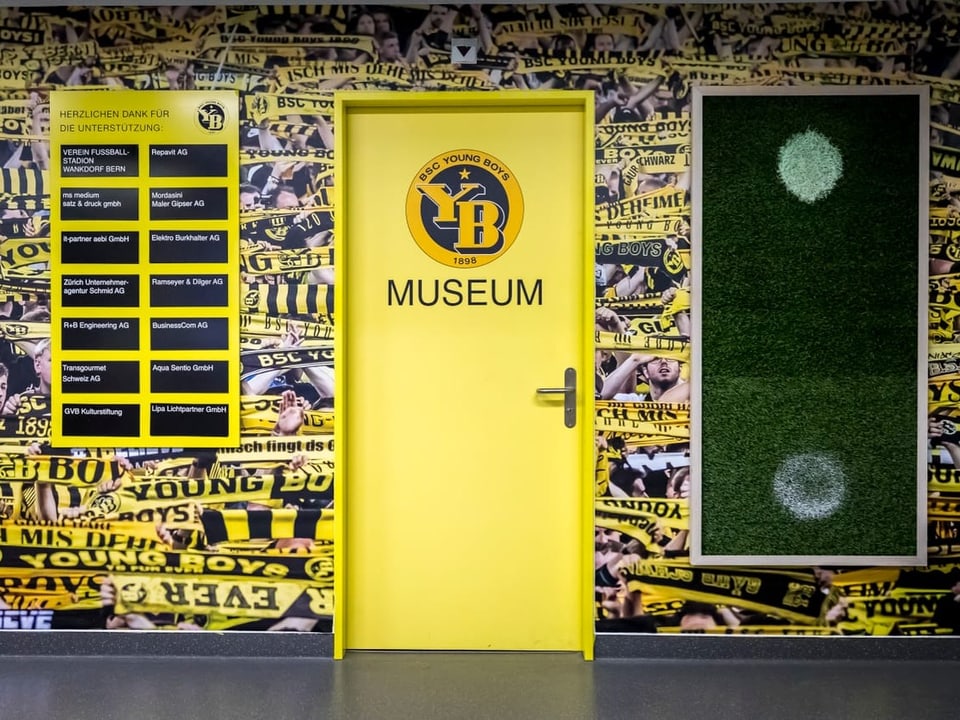 Eine gelbe Tür mit der Aufschrift «YB Museum». Die Wand rund um die Tür zeigt ganz viele gelb-schwarze YB-Schals.