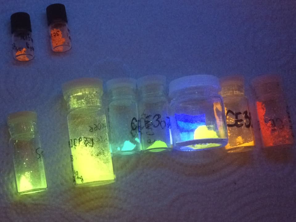 Mehrere Glasbehälter mit leuchtendem Pulver in verscheidenen Farben.
