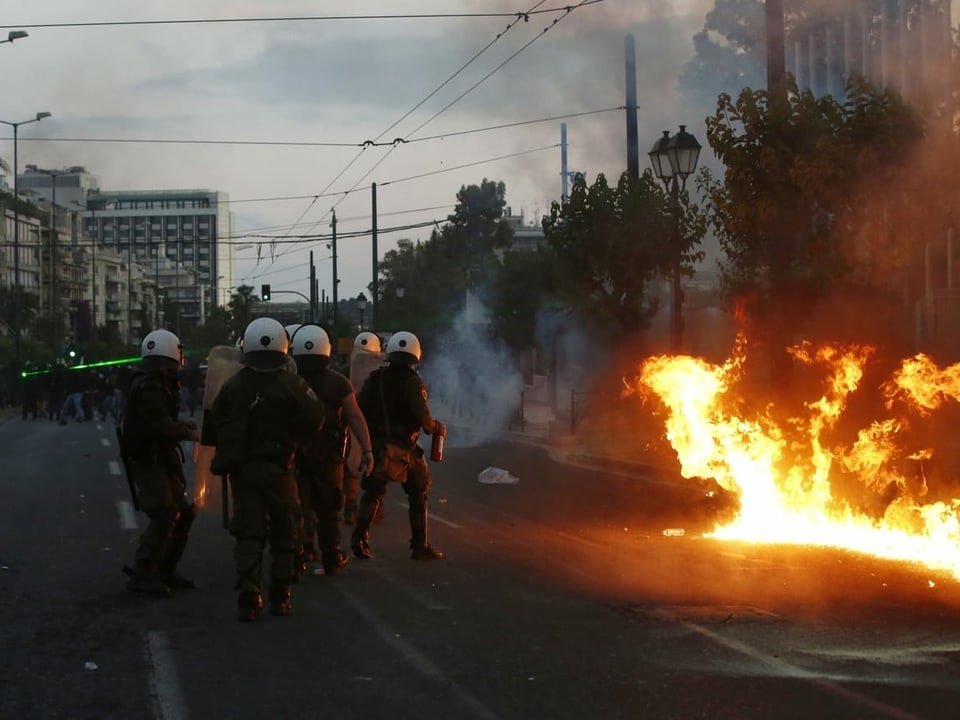Ausschreitungen in Athen – Polizisten stehen auf einer Strasse neben Flammen. 