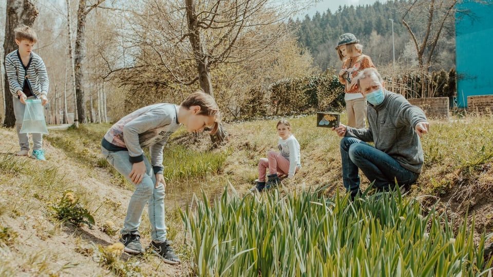 ein Mann ist mit mehreren Kindern im Garten und erklärt etwas