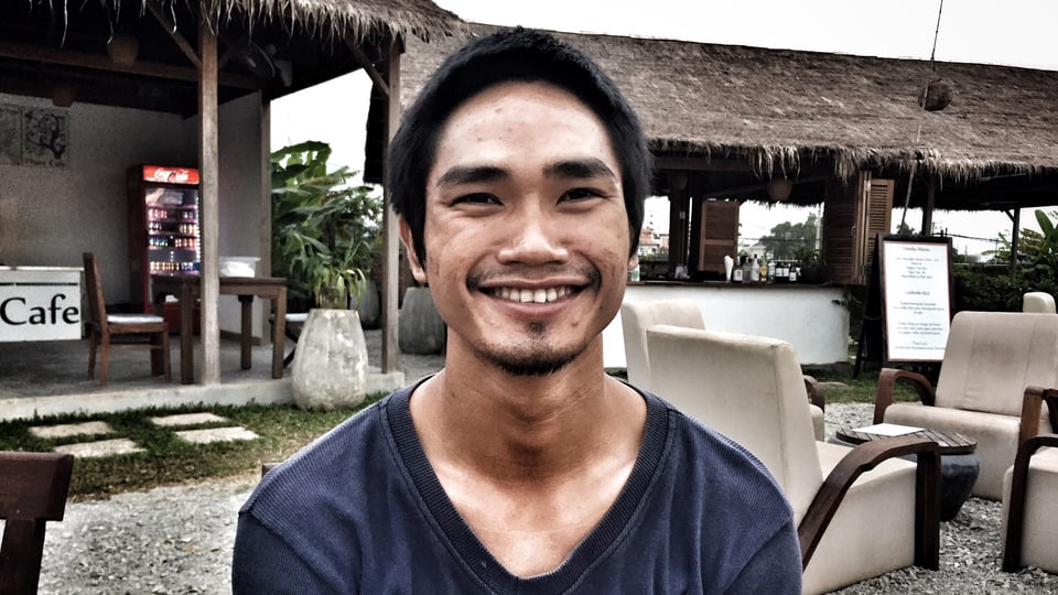 Ein junger Kambodschaner in blauem Pullover lächelt in die Kamera.