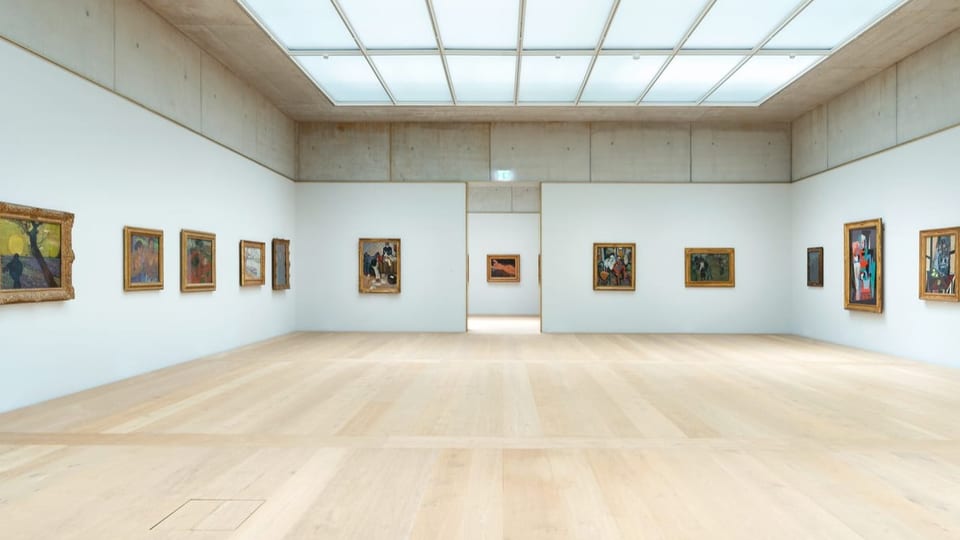 Heller Raum, heller Holzboden, weisse Wände mit Gemälden.