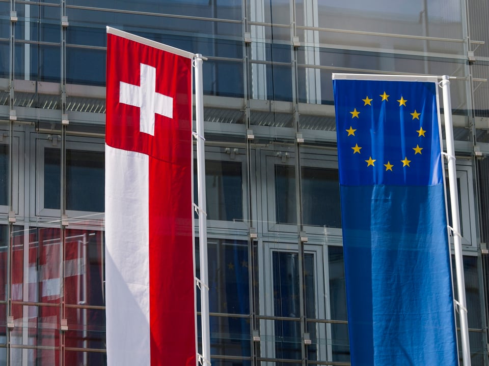 Die Schweizer und EU-Flagge nebeneinander vor einem Glasgebäude. 