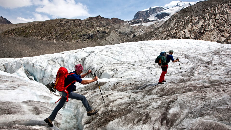 Zwei Wanderer auf dem Gornergletscher bei Zermatt. Einer springt über eine Spalte.
